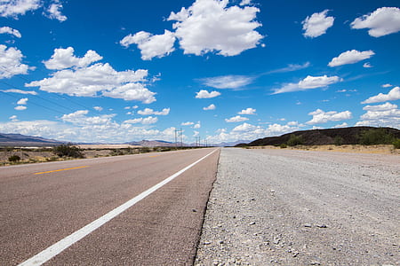 narrow asphalt road under white and blue sky thumbnail