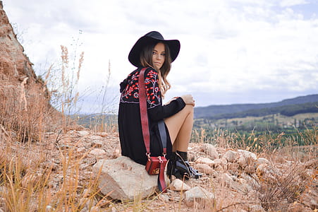 woman sitting on beige stone with view of valley below during daytime thumbnail