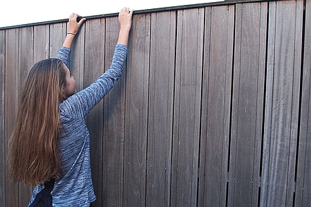 woman climbing brown wooden fence outdoor during daytime thumbnail
