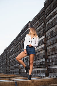 woman wearing white dress shirt and blue jeans standing on wood beams thumbnail