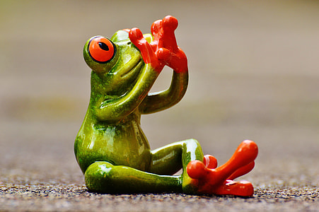 sitting green and red ceramic frog on gray concrete pavement thumbnail