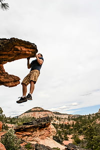 man hanging on rocky cliff under white clouds during daytime thumbnail