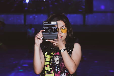 woman holding instant camera facing the direction of the camera inside dim-lighted room thumbnail