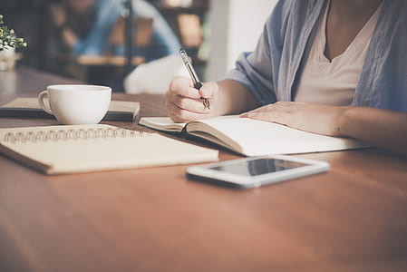 Woman Writing on a Notebook Beside Teacup and Tablet Computer thumbnail