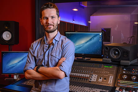 man wearing blue button-up t-shirt standing in front of recording studio equipment thumbnail