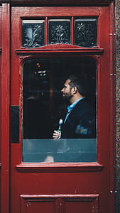 man holding glass bottle standing in front of brown wooden door thumbnail
