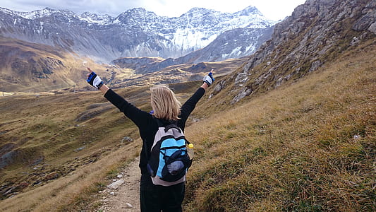 woman carrying backpack at the field near the mountains during day thumbnail