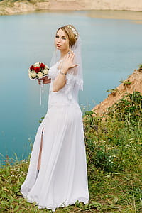 Woman Wearing White Wedding Gown While Standing on Cliff Near River thumbnail