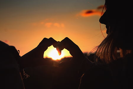 silhouette of man and woman making heart sign with both hands at sunset thumbnail