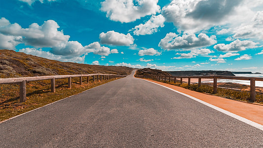concrete road beside body of water under cloudy sky thumbnail