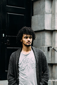 man in grey crewneck T-shirt and grey cardigan standing on black door thumbnail