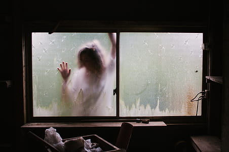 person wearing white shirt leaning on frosted glass window view from dim-lighted room thumbnail