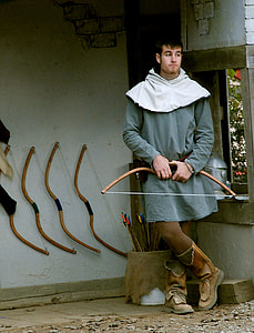 man holding bow standing near four racked bows thumbnail