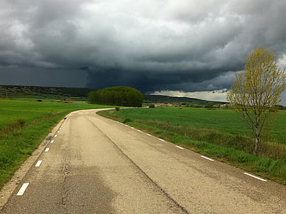 gray road near green grass field under nimbus clouds during daytime thumbnail