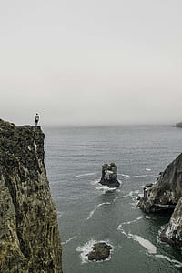 man standing on cliff under grey sky thumbnail