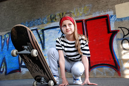 girl stepping on black skateboard near wall during daytime thumbnail
