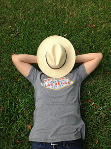 person in gray shirt lying on grass field with brown sun hat on face thumbnail