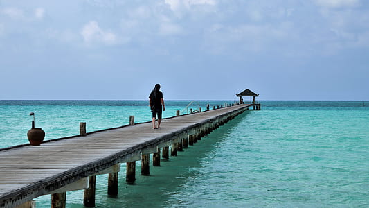 man walking on wooden dock on body of water thumbnail