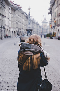 woman wearing scarf standing in open area surrounded by buildings thumbnail