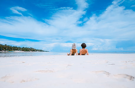 two women sitting on seashore during daytime thumbnail