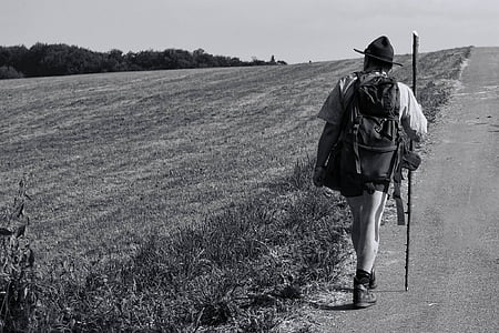 grayscale photo of man in hiking set walking along the pathway thumbnail