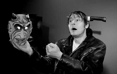 grayscale photo of man holding devil mask thumbnail