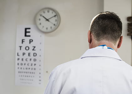 Doctor Facing Snellen Chart Beside Analog Wall Clock Displaying 10:10 thumbnail