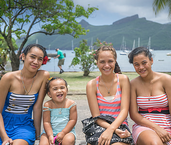 three woman and girl sitting near body of water thumbnail