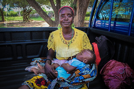 woman wearing yellow top carrying baby sitting on black truck bed thumbnail
