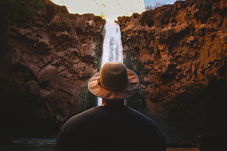 man wearing brown hat standing fronting waterfalls thumbnail