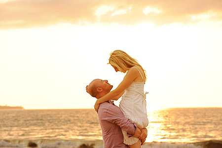 man carrying the woman near the body of water photography thumbnail