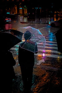 person standing near pedestrian lane while carrying an umbrella during night thumbnail