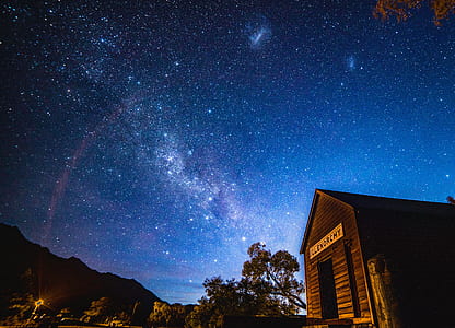 brown wooden cabin overlooking mountains and milky way at night time thumbnail