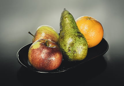 two apples, avocado, and orange on black ceramic plate thumbnail