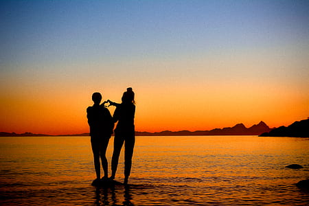 silhouette of two person doing heart hand sign on body of water thumbnail