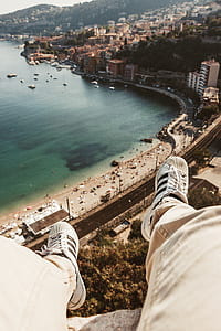 person wearing adidas Superstar sitting on gray concrete in front of buildings and body of water thumbnail