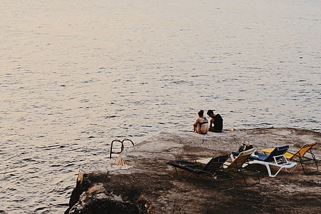 couple sitting near body of water during daytime thumbnail