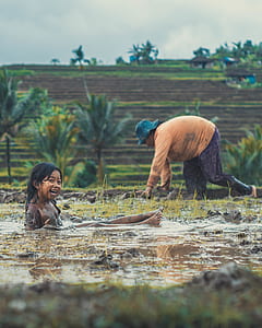 girl playing in puddle of mud during daytime thumbnail
