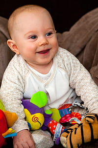 baby wearing white and brown long-sleeved shirt holding plush toys thumbnail