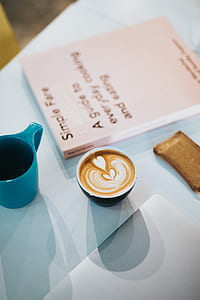 black ceramic mug with latte art near book an d green mug thumbnail