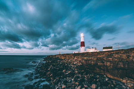 white lighthouse near buildings and cliff photo thumbnail