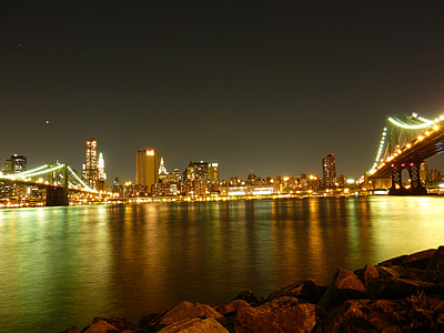 rocks beside calm water near city buildings with golden lights during nighttime thumbnail