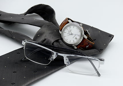 closeup photo of grey framed eyeglasses near round silver-colored analog watch on grey necktie thumbnail