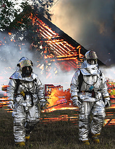 two fireman walking on the grass with burning fire house at the back thumbnail