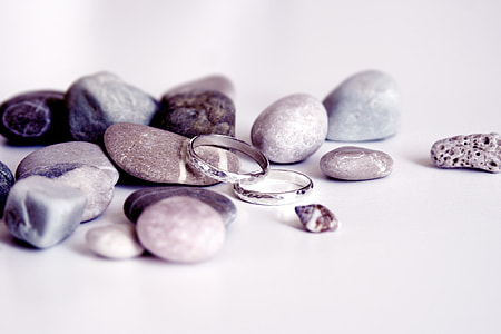 pair of silver-colored wedding band on top of white surface beside gray stone thumbnail