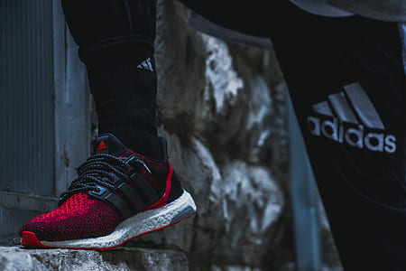 person wearing black and red adidas sneaker stepping on gray stone thumbnail