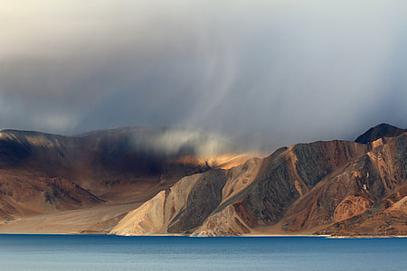 brown mountain near ocean under white sky thumbnail