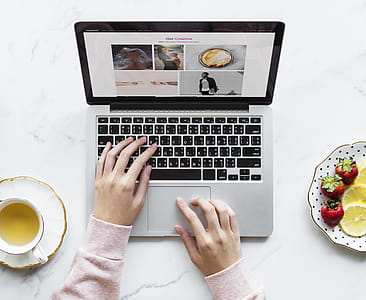 Person Using Black and Gray Laptop Beside White Ceramic Cup and Saucer on White Table thumbnail