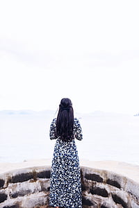 woman standing beside concrete wall facing body of water during daytime thumbnail