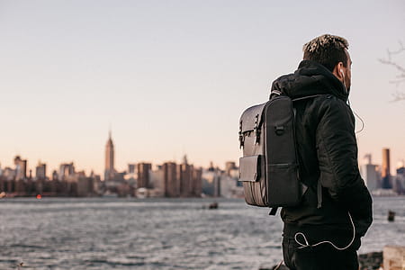 Man Wearing Black Bubble Jacket and Black Leather Backpack Near Bay thumbnail